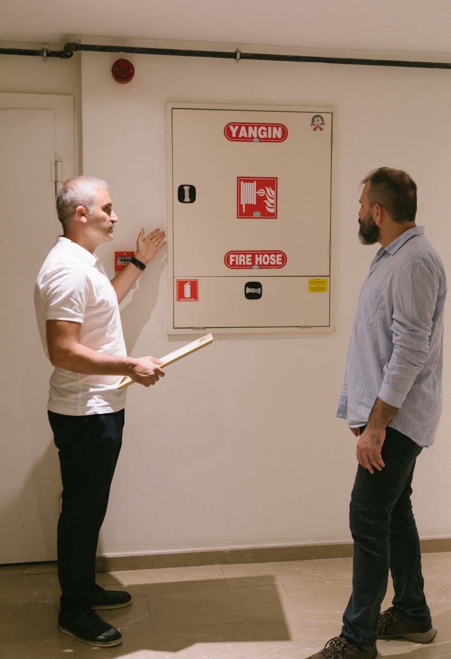 two men standing near a fire hose metal cabinet